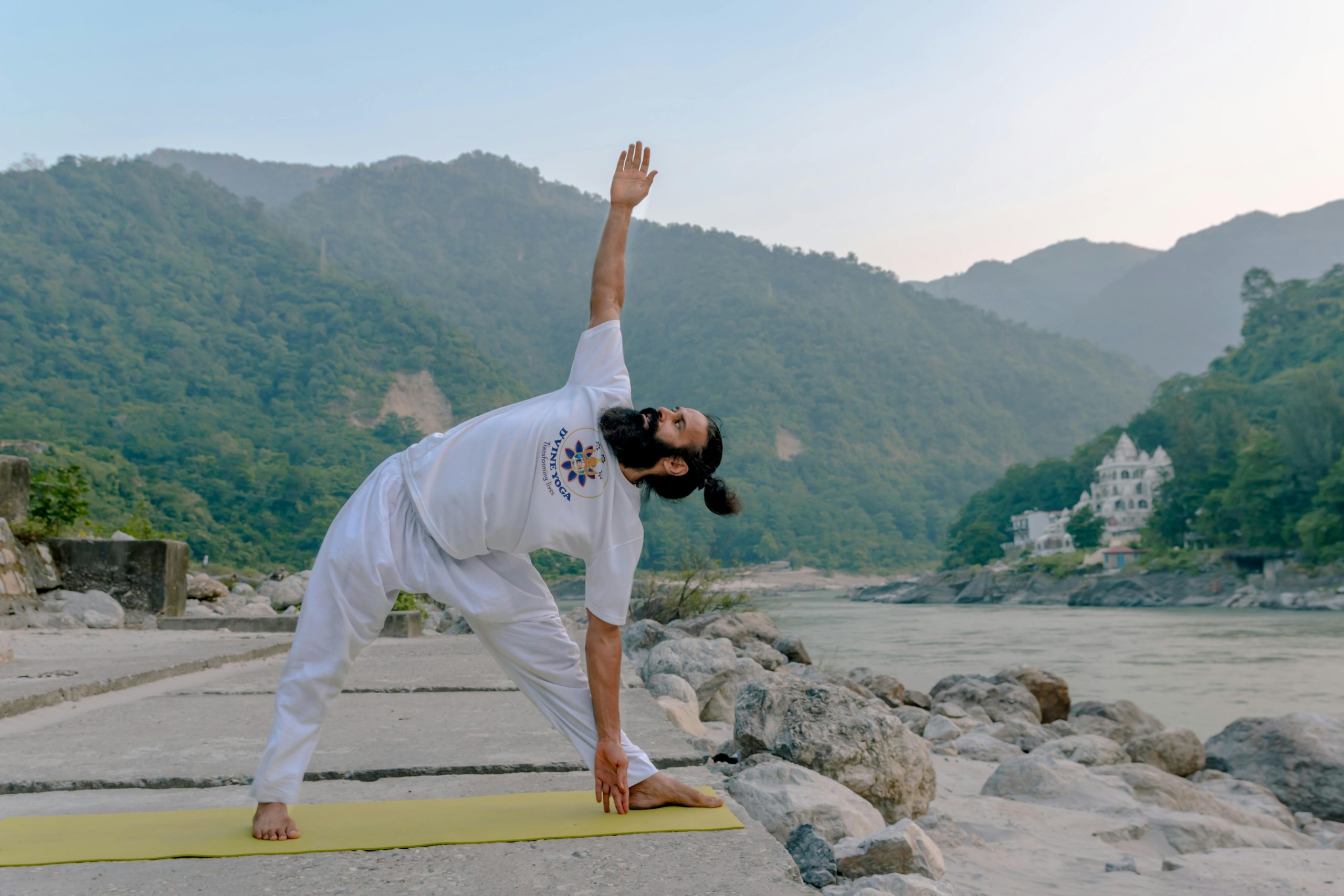 Man practicing yoga by the Ganges in Rishikesh with a serene mountain backdrop.